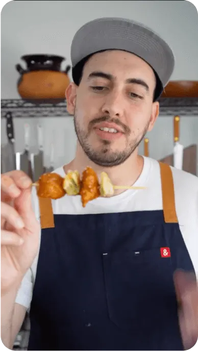 Creator with mustache and hat in professional chefs kitchen looks at bibigo dumplings on a skewer
