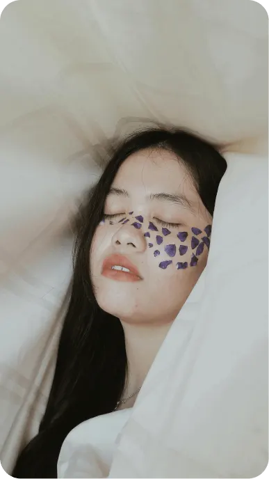 Woman with purple face makeup sleeps in white sheets