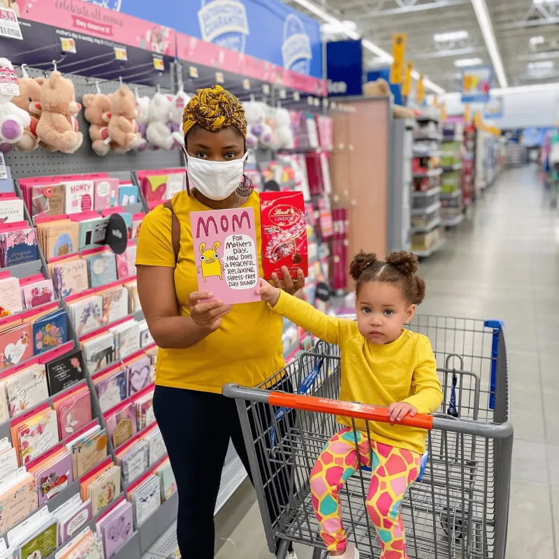 Woman in mask poses with her child and a greeting card in Walmart