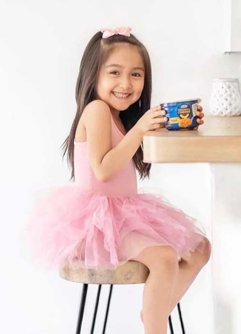 Small child in a tutu sitting at table with Kraft mac and cheese