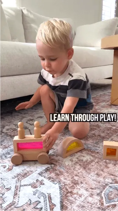 Boy plays with wooden toy on living room floor with text overlay reading Learn Through Play