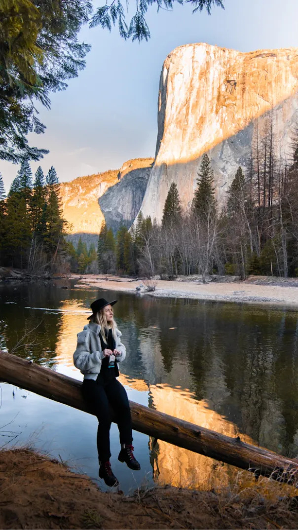 Woman in fur coat and black hat eats packaged snack bar in front of a beautiful natural scenery