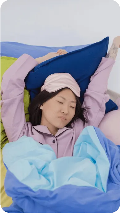 Woman with pink silk pajamas and eye mask sleeps in bed with blue bedding