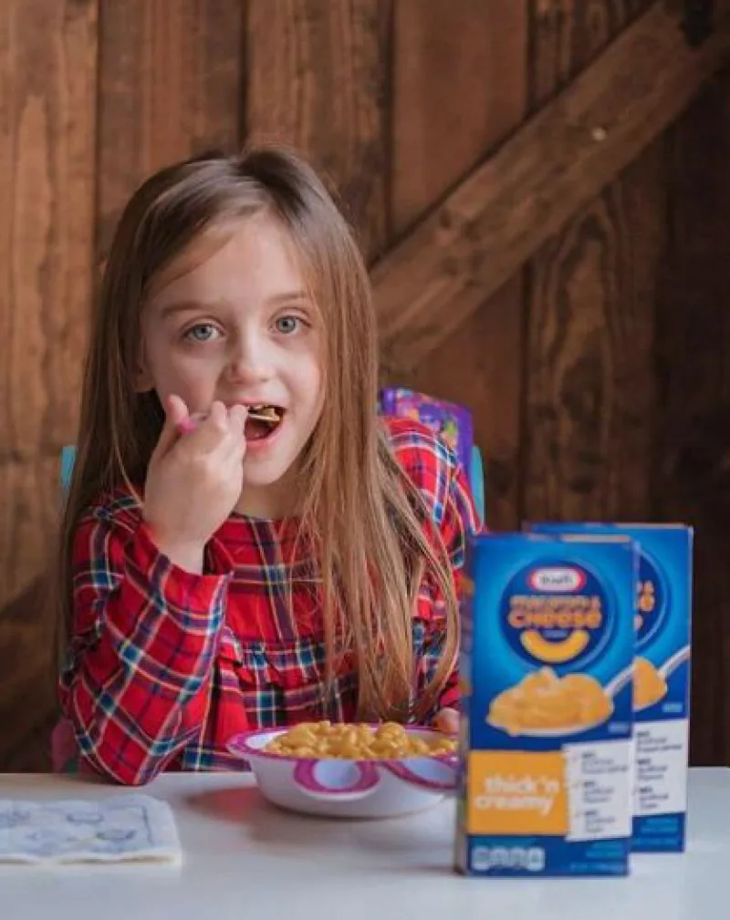 Girl looking into camera while eating a bowl of Kraft mac and cheese