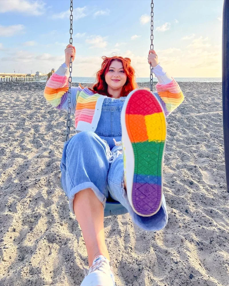 Creator on swing set on the beach wearing Sperry PFLAG rainbow bottom shoes