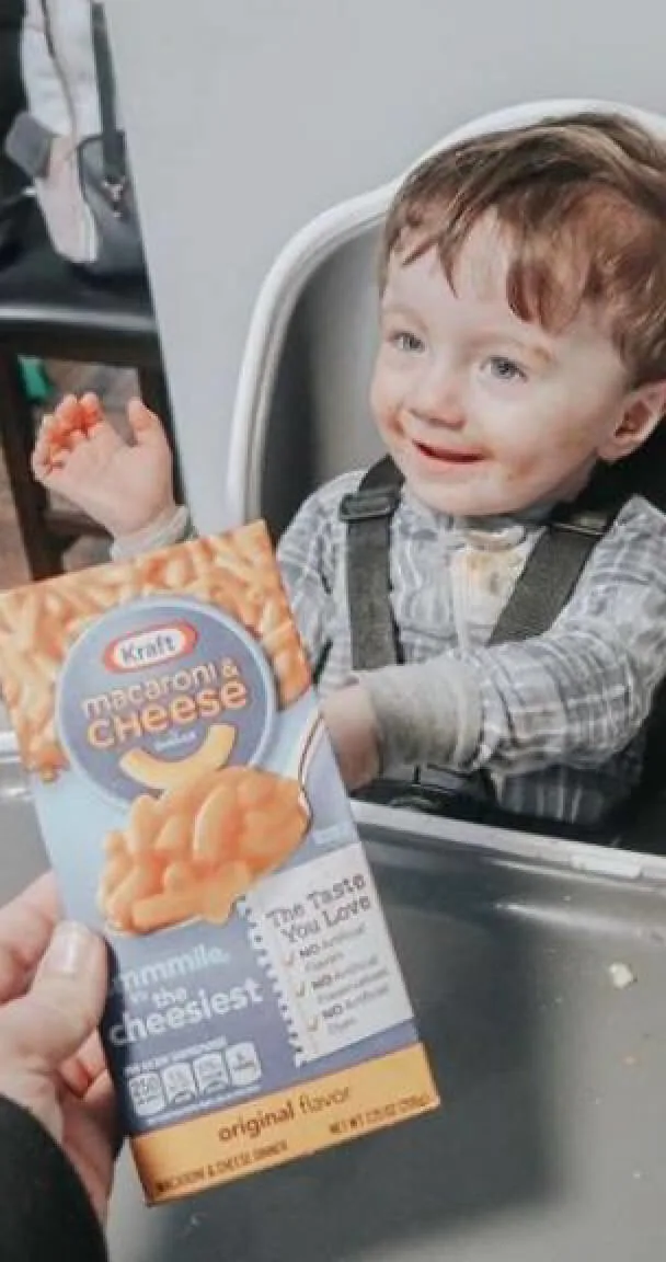 Baby in a highchair with a box of Kraft mac and cheese