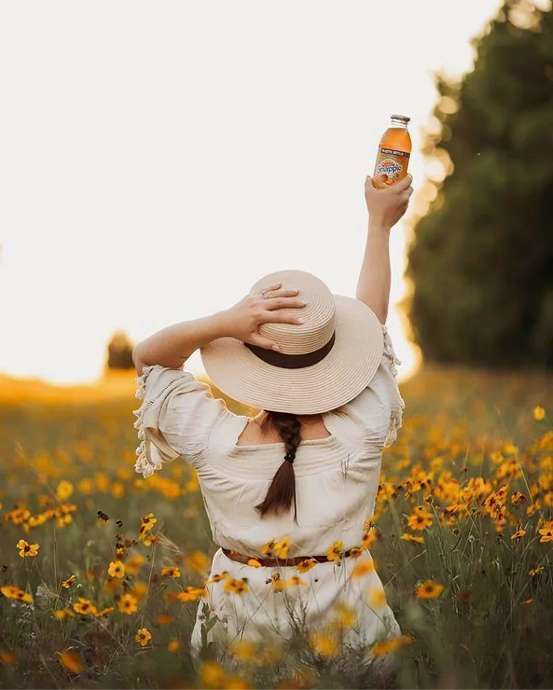 Woman influencer in a field of yellow flowers at sunset with her right arm straight up holding a Snapple drink