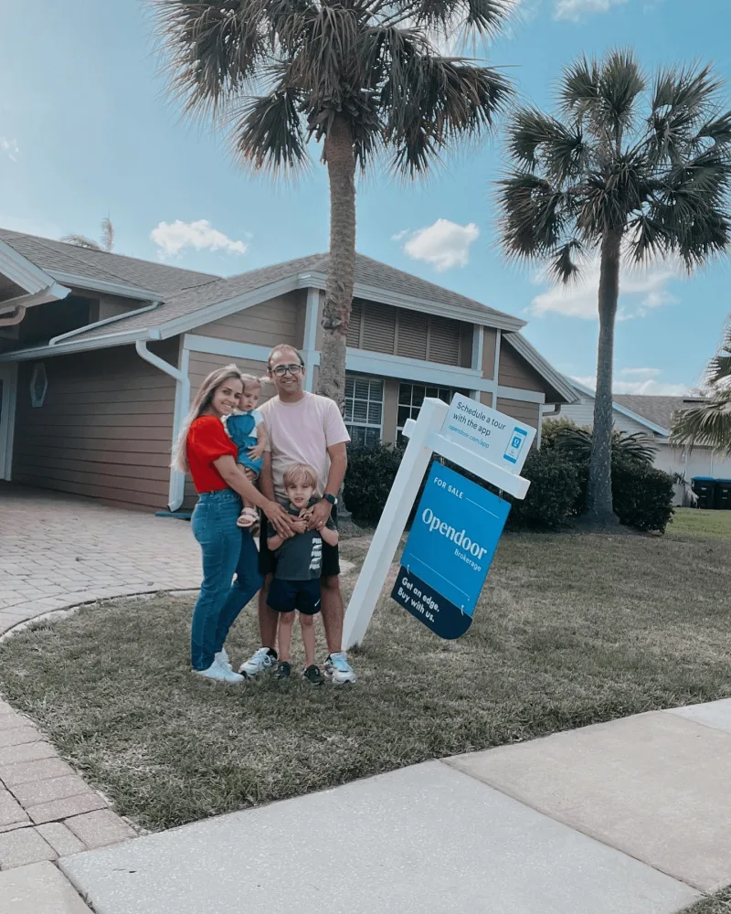 Young family poses in front of home with OpenDoor sign next to key campaign results