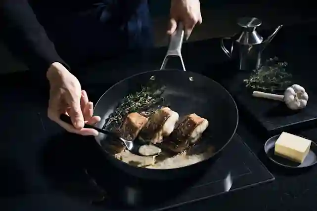 Fiskars Taiten pannulla paistetaan kalaa ja sitä voidellaan kastikkeella samalla.