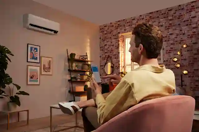 Mies istuu nojatuolilla, älypuhelin kädessä, jonka ruudulla näkyy huoneen lämpötila ja ilmalämpöpumpun asetuksia.