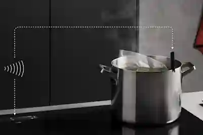A steaming stainless steel pot on an induction cooktop, displaying a wireless connection symbol.