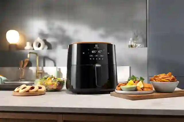 Airfryer ylväänä keittiön tasolla. Ympärillä erilaisia sillä valmistettuja herkkuja.