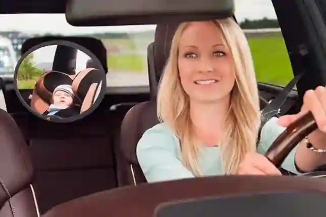 Auton kuljettaja katsoo peilistä Hauckin turvaistuimessa nukkuvaa vauvaa ja ajaa autoa.