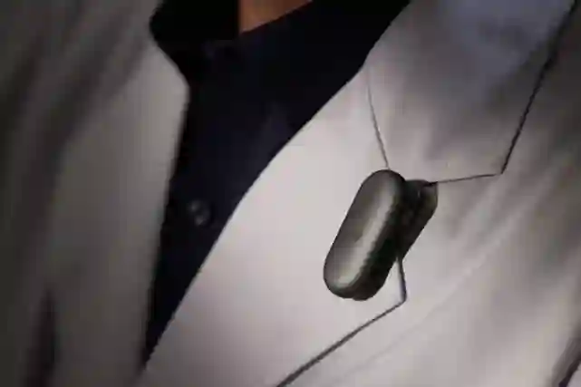 Black wireless Bluetooth headset clipped to the pocket of a person's light-colored jacket.