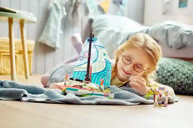 Punatukkainen tyttö leikkii lattialla makoillen lego purjeveneellä. Tutustu Verkkokauppa.comin leluihin!
