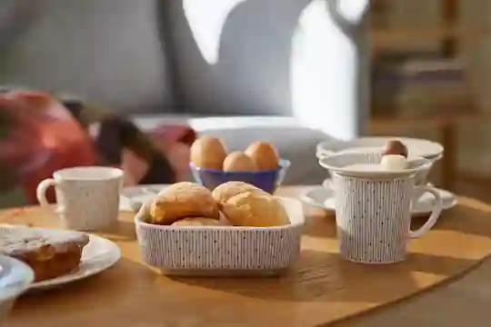 Katettu aamiaispöytä. Kananmunia kupissa, leipiä vuoa'assa ja kahvikuppeja.