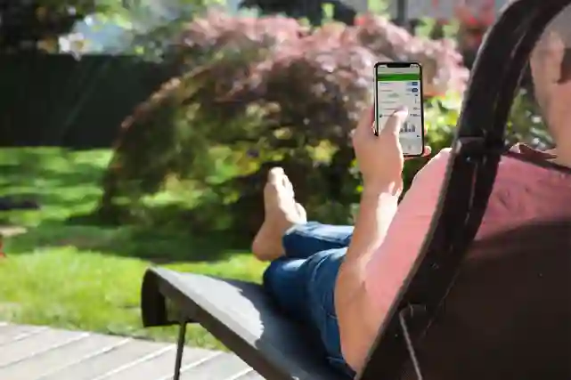 Mies ottaa aurinko tuolissa ja katsoo puhelimesta kotiautomaatio asetuksia. Lue lisää miten säästät energiaa kotiautomaation avulla!