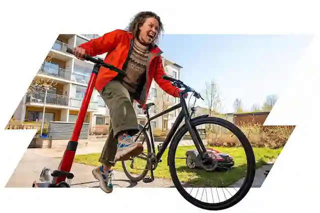 Keväinen piha-alue, jossa henkilö liikkuu samanaikaisesti polkupyörällä ja sähköpotkulaudalla. Taustalla asuinrakennuksia, vihertyvää nurmikkoa ja kirkasta kevätaurinkoa, etualalla modernia kaupunkimiljöötä ja selkeä keväinen tunnelma.