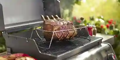 Grillat lammstekt på metallställning på Spirit-gasgrillens galler, med trädgård och kryddor i bakgrunden.
