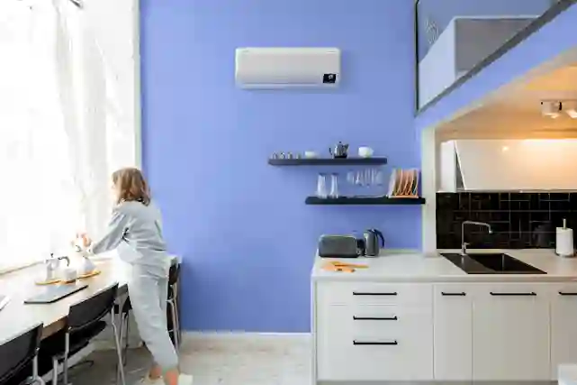 Nainen asettelemassa kukkia keittiössä, keittiön seinällä ilmalämpöpumppu kuivuvien tiskien yläpuolella.