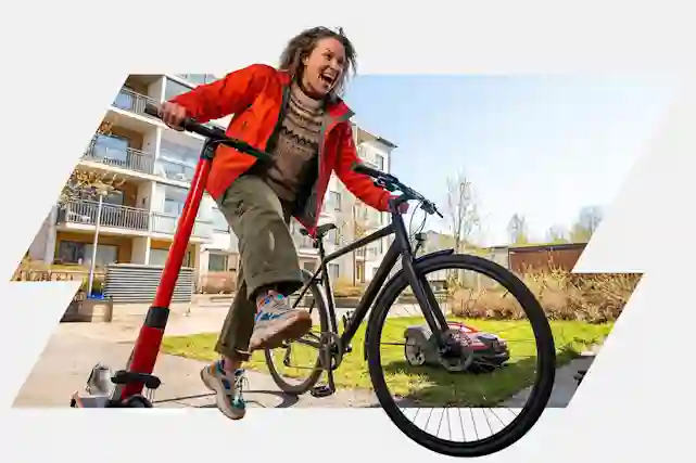 Keväinen piha-alue, jossa henkilö liikkuu samanaikaisesti polkupyörällä ja sähköpotkulaudalla. Taustalla asuinrakennuksia, vihertyvää nurmikkoa ja kirkasta kevätaurinkoa, etualalla modernia kaupunkimiljöötä ja selkeä keväinen tunnelma.