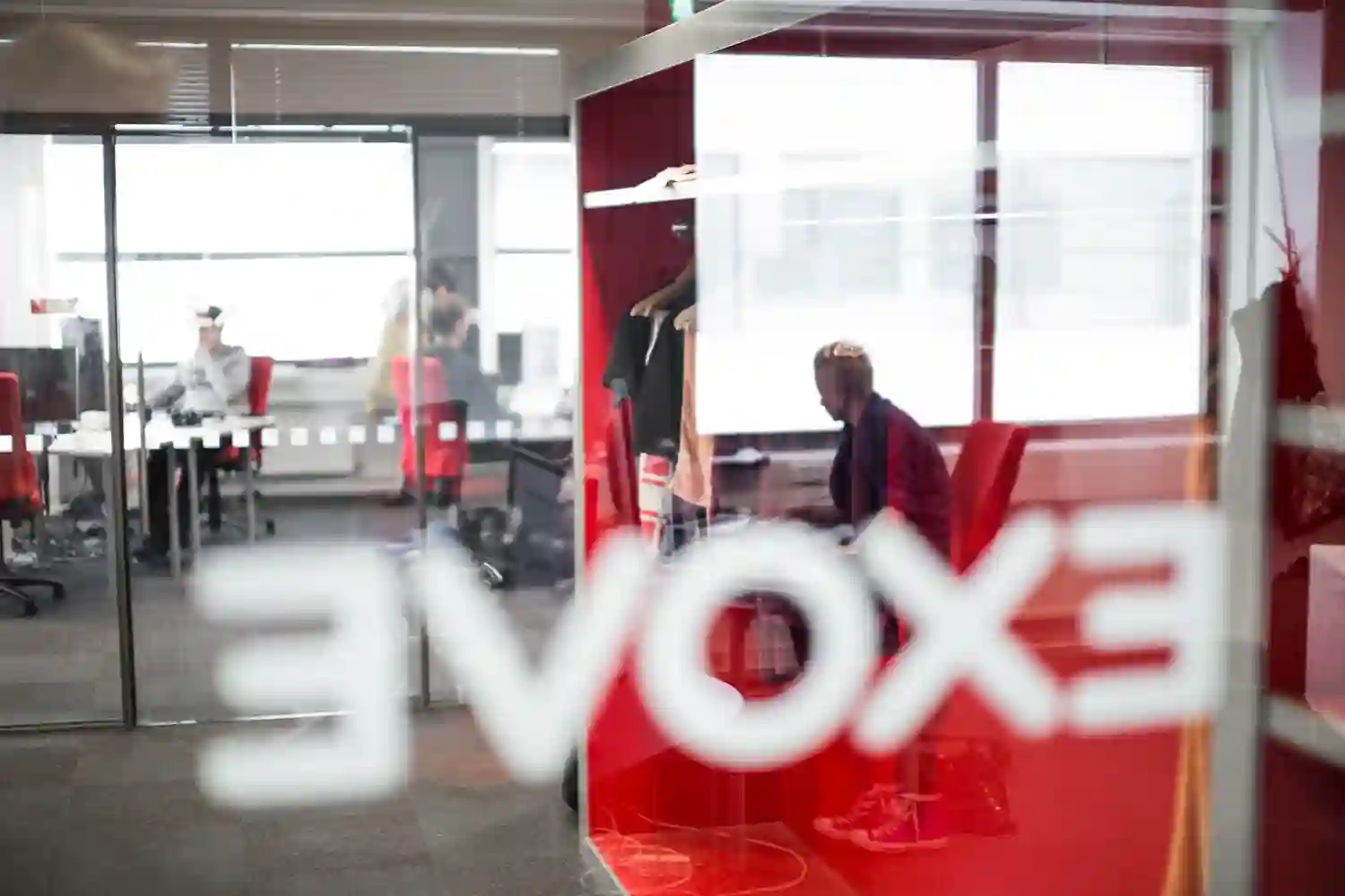 Exoven logo väärinpäin sumeana lasiovessa, jonka takana näkyy punaharmaata toimistotilaa.