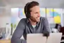 Työntekijällä on Jabran kuulokkeet päässä ja keskustelee hymyillen työpöydän ääressä.