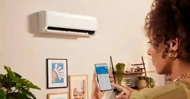 Nainen puhelimella, jonka näytöllä ilmalämpöpumpun asetukset ja huoneen lämpötila.