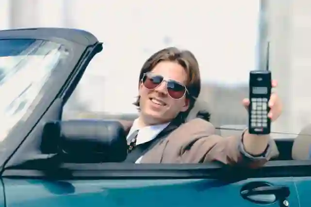 Juppi Jyrki esittelee GSM-puhelintaa istuessaan avoautossaan.