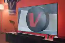Kuvassa olohuone jossa seinällä roikkuu verkkiksen pelipaita. Televisiossa lähikuvassa mailan lapa ja kiekko jossa v-logo.