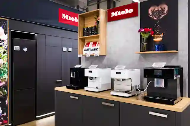 Miele-butikens utställningsområde med svarta och vita kaffemaskiner på träbänk, röda Miele-skyltar på väggen.
