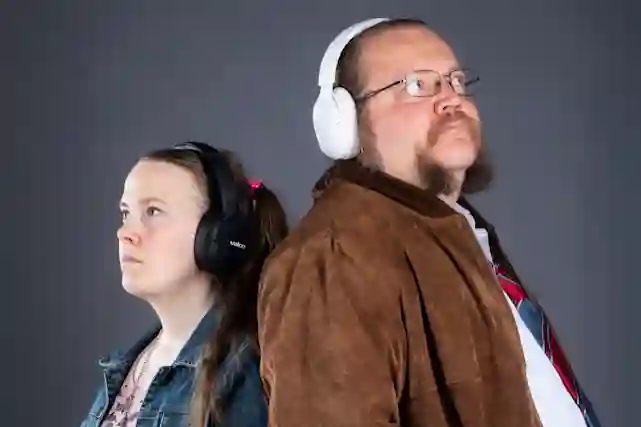 A woman and a man stand back-to-back wearing wireless Valco headphones against a gray background.