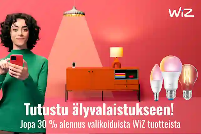 Nainen älypuhelimella vaaleanpunaisessa huoneessa, jossa oranssi lipasto ja WiZ-älylamppuja. Jopa 30 % alennus valikoiduista WiZ tuotteista.