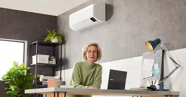 Nainen työpöydän ääressä villapaita päällä, ilmalämpöpumpun alla.