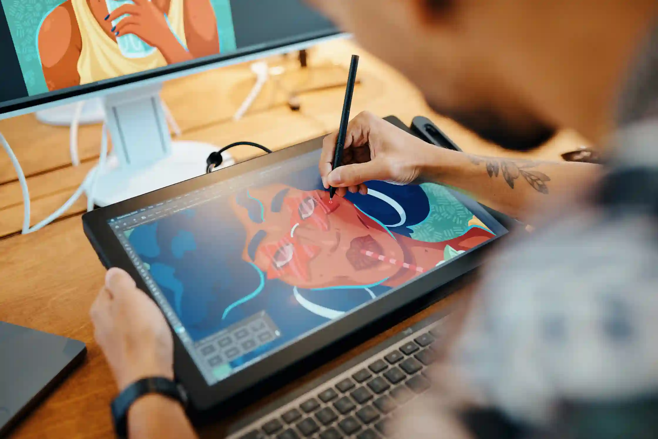 A person draws digital illustrations on a Wacom drawing tablet with a pen at a desk.