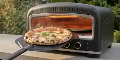 En svart pizzaugn utomhus på ett bord, med en pizza margherita med basilika som gräddas inuti.