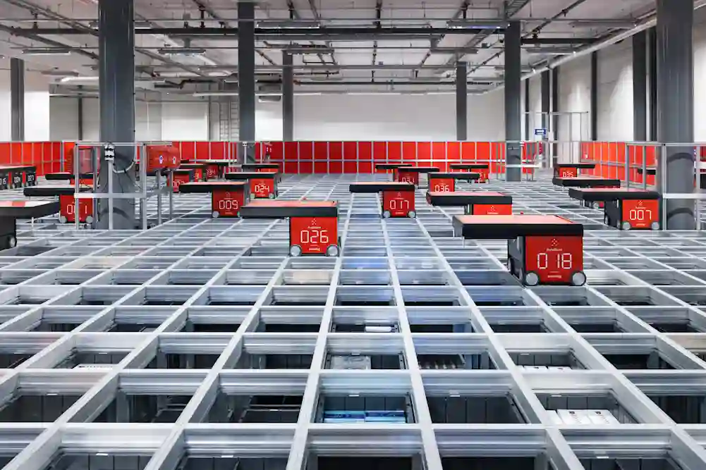 AutoStore varastoautomaatti kuvattuna ylhäältäpäin Helsingin varastossa. Pyörillä varustetut robotit liikkuvat ja kuljettavat tuotteita ristikkomaista rakennetta pitkin.