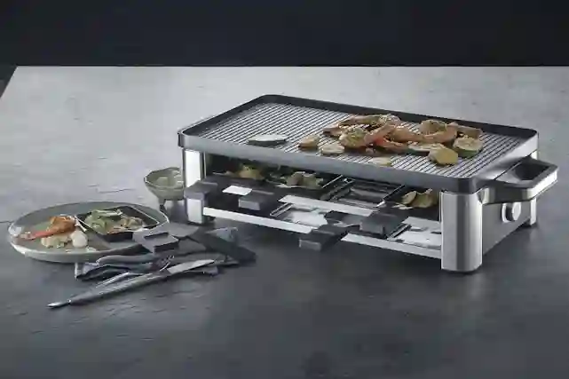 WMF Lono -raclettegrilli keittiöpöydällä. Siinä on tulossa kaikilla tasoilla ruokaa.