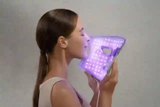 Nainen käyttää violettia LED-valohoitonaamiota kasvoillaan harmaata taustaa vasten.