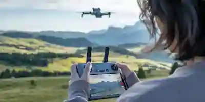 Henkilö ohjaa dronea kaukosäätimellä maisemassa, jossa näkyy peltoja ja metsiä.