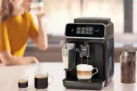 Philips-espressokone valmistaa cappuccinoa keittiön työtasolla, vieressä kahvipapuja lasipurkissa.