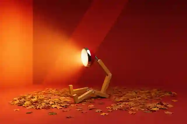 Röd bordslampa med träfot bland höstlöv mot röd bakgrund.