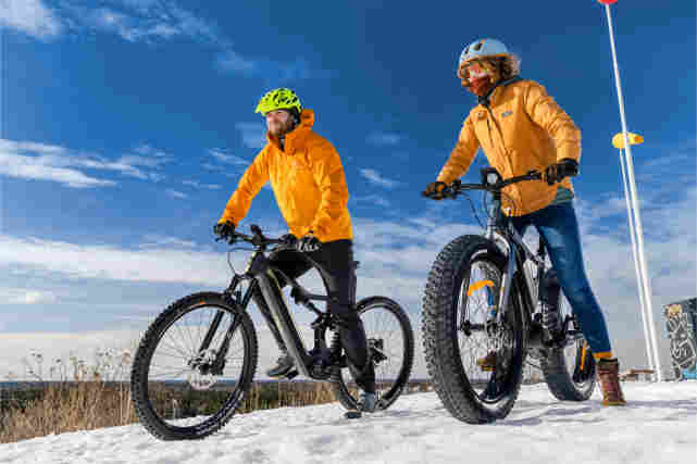 Kaksi talvipyöräilijää lumisessa maisemassa.