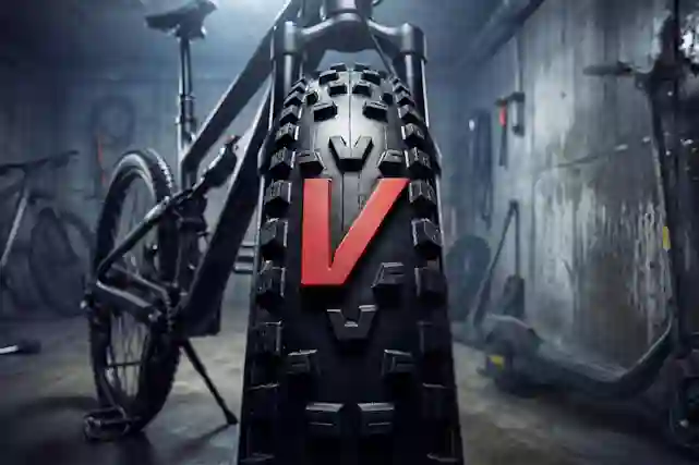 Pyörävarastosta kuva, jossa lähikuvassa polkupyörän renkaassa oleva punainen V-logo, joka on yksi iso kumiosa renkaassa. Taustalla sähköskuutti ja polkupyörä. Tutustu valikoimaan.