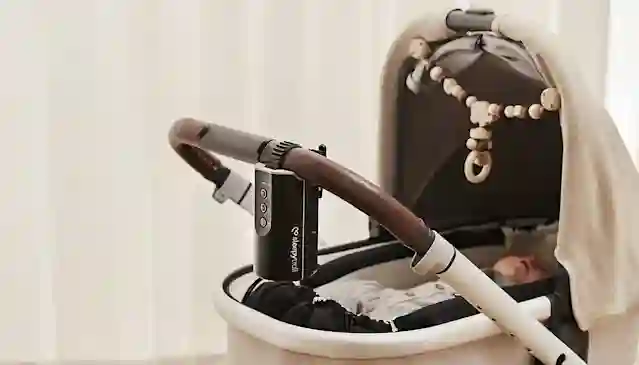 Vauva nukkuu vaunuissa, joiden työntöaisassa on kiinni Sleepytroll -lastenvaunujen keinuttaja