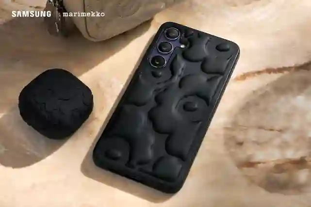 Mustat Samsung X Marimekko embossed kuoret puhelimessa ja puhelin on pöydällä. Vieressä Samsung Budsit jossa myös samanlaiset suojakuoret