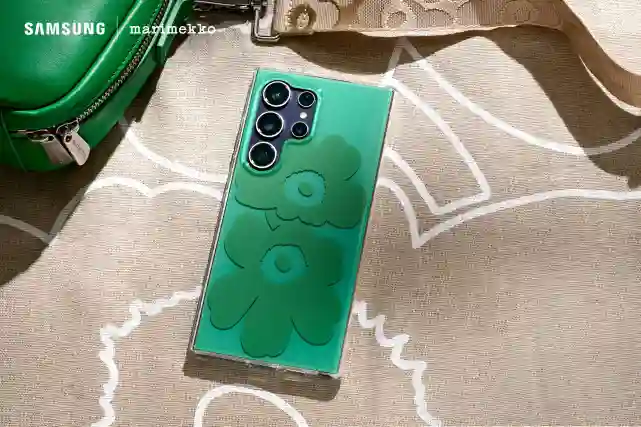Kuva Samsung x Marimekko yhteistyössä tehdyistä kuorista puhelimessa. Siinä on vihreää Unikko-kuosia läpinäkyvässä kuoressa. Taustalla Marimekon laukku ja pöytäliina.