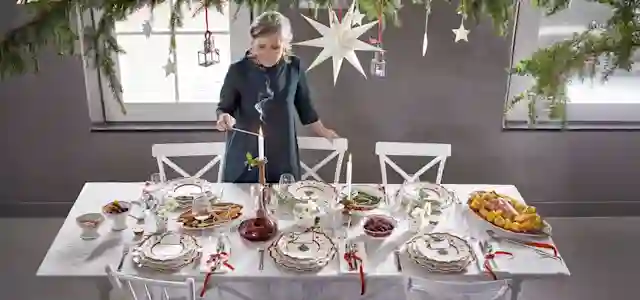Henkilö koristelee ruokapöytää upealla ja runsaalla joulukattauksella. Kuvaa on jatkettu tekoälytuökalulla.