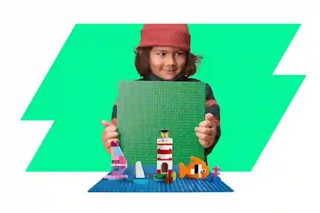 Lapsi pitää vihreää LEGO-alustaa Lego-rakennelman taustalla ja myhäilee.