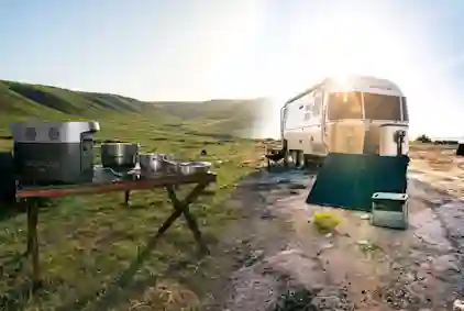 Virta-asema, asuntoauto ja keittiötarvikkeita kesämaisemassa.